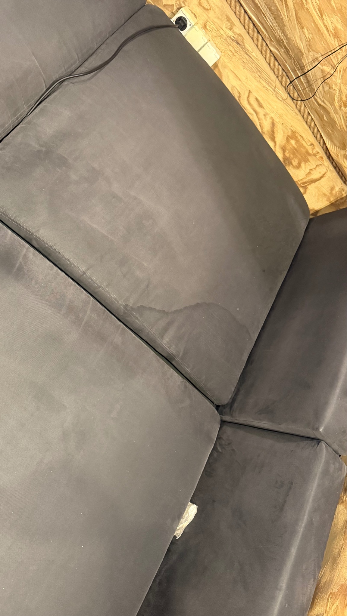 Szare, modułowe siedzisko z plamą, widoczne z góry pod kątem. Fragment ściany z płyty OSB w tle. Widoczny kabel i gniazdko elektryczne.