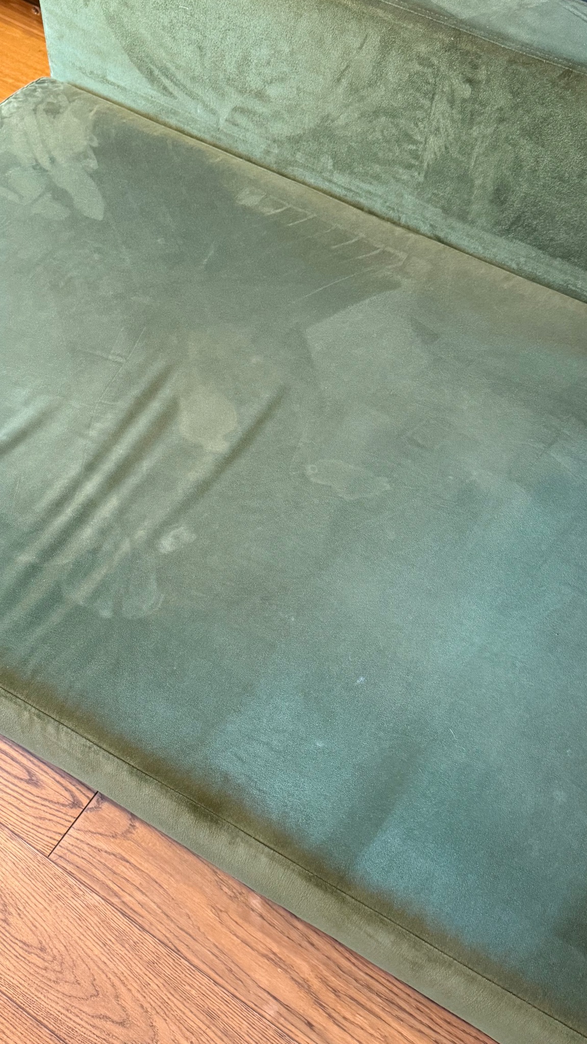 Zielona, welurowa kanapa z widocznymi plamami na siedzisku, częściowo na drewnianej podłodze. Usługa prania kanap w Kościelisku.