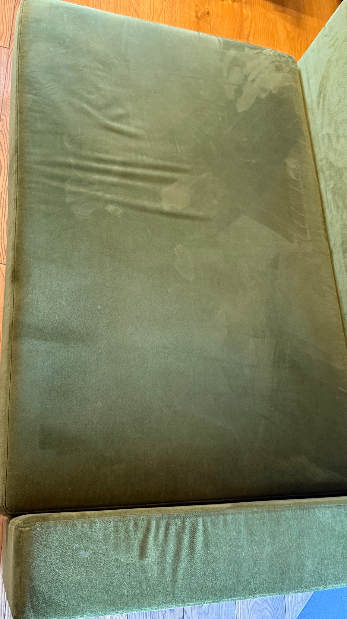 Zielona, welurowa kanapa z widocznymi plamami i zabrudzeniami na siedzisku. Widok z góry, ukazujący fakturę materiału i potrzebę czyszczenia.