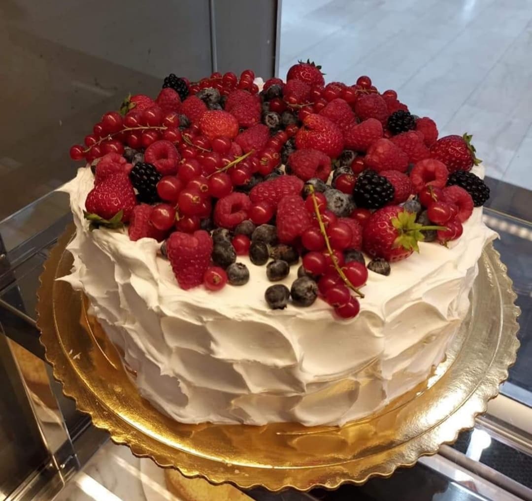 Tort z białym kremem i obficie ułożonymi świeżymi owocami: truskawkami, malinami, porzeczkami i jeżynami, na złotej paterze.
