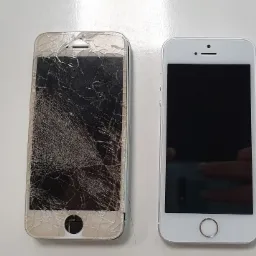 Dwa telefony iPhone 5s leżące obok siebie na białym tle; jeden z mocno potłuczonym ekranem, drugi w idealnym stanie.