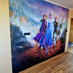 REMONTOZNAWCY - Fototapeta z motywem z 'Krainy Lodu' na ścianie w pokoju, widoczne brązowe panele podłogowe i gniazdka elektryczne na ścianie pod tapetą.