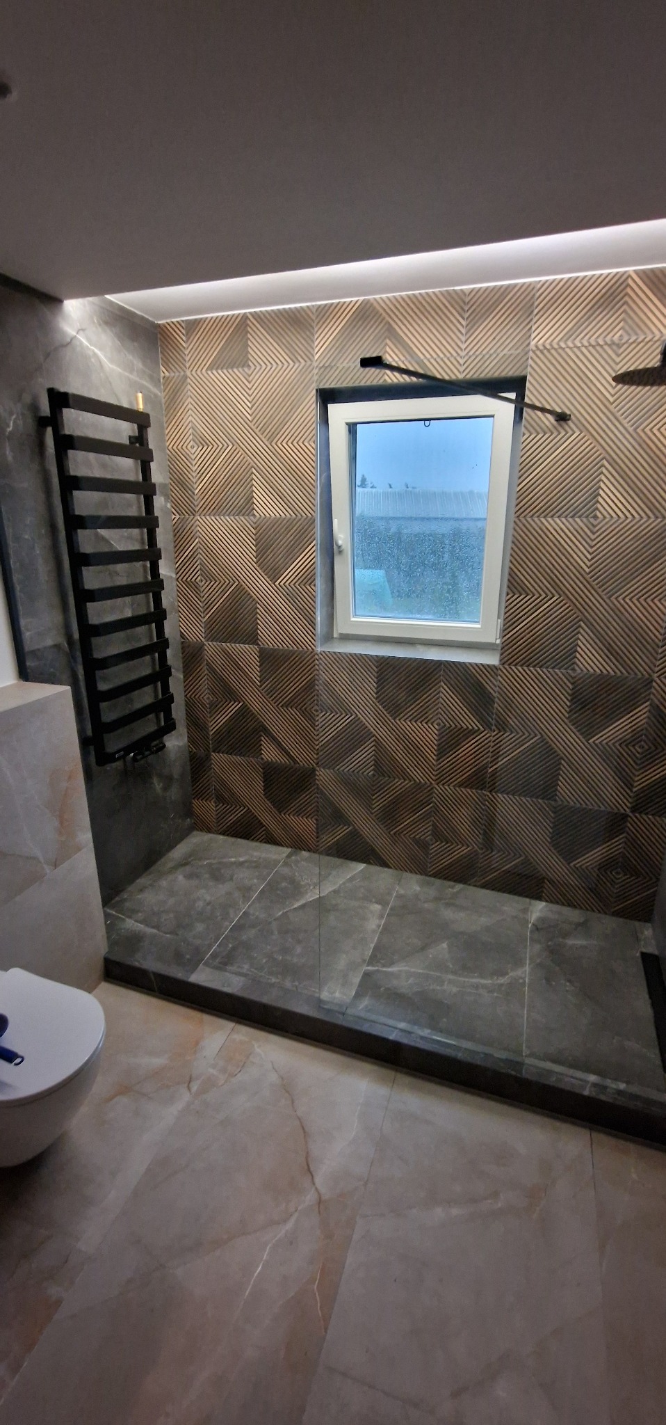 Nowoczesna łazienka z kabiną typu walk-in,  płytki w geometryczne wzory na ścianie,  grzejnik drabinkowy w kolorze czarnym i małe okno.