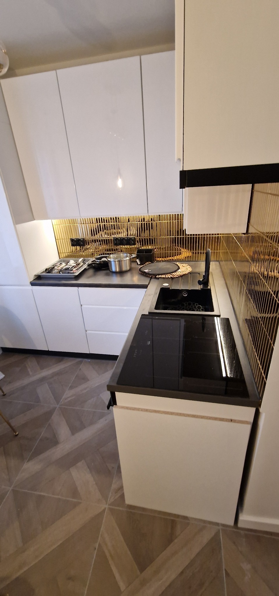 Biała kuchnia z złotym panelem w Inowrocławiu. Nowoczesna zabudowa, płyta indukcyjna i designerska armatura. Uwagę przykuwa wzór na podłodze.