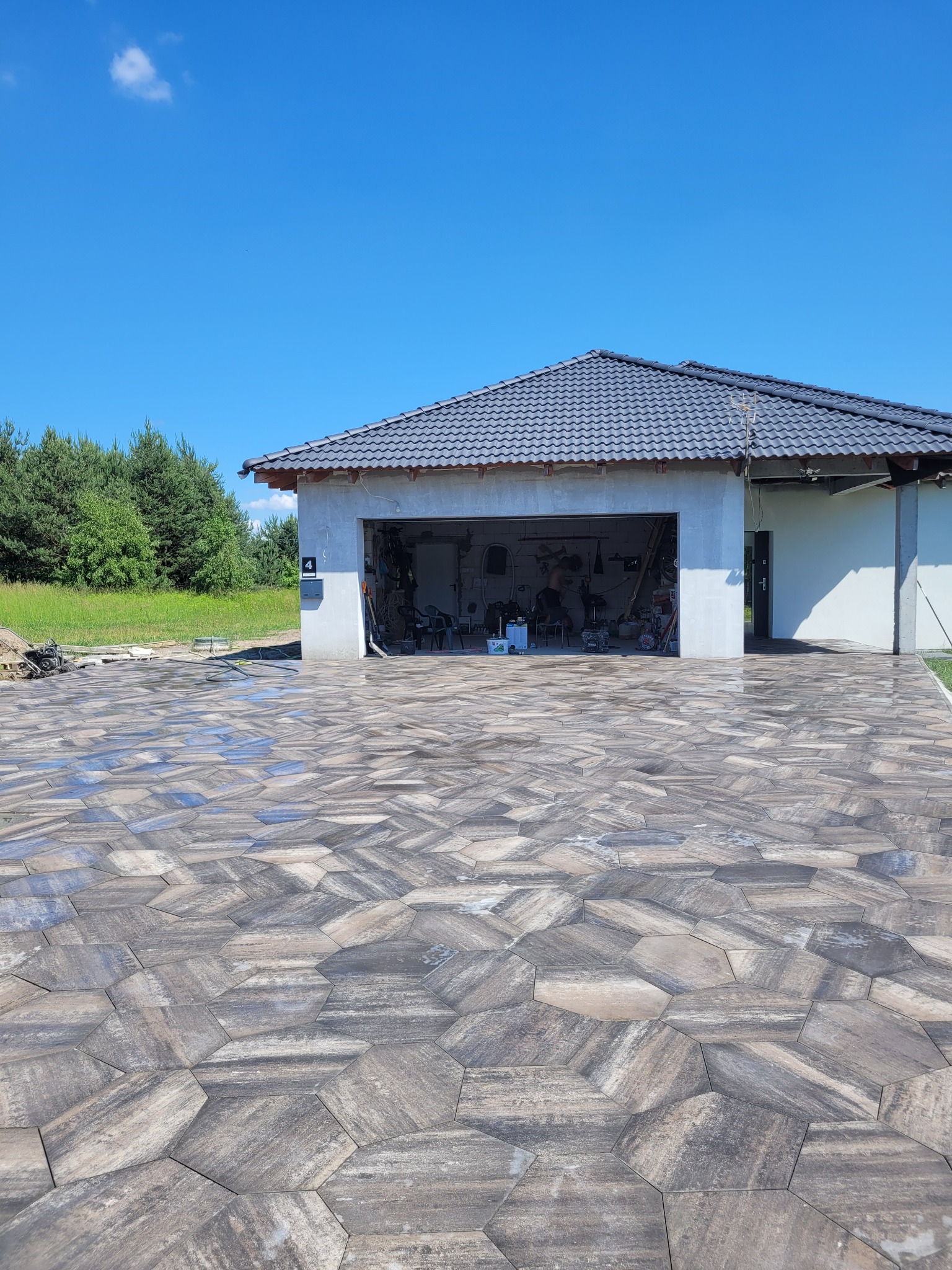 Nowoczesny dom z garażem i wyłożonym kostką brukową podjazdem o heksagonalnym wzorze w odcieniach szarości i beżu.