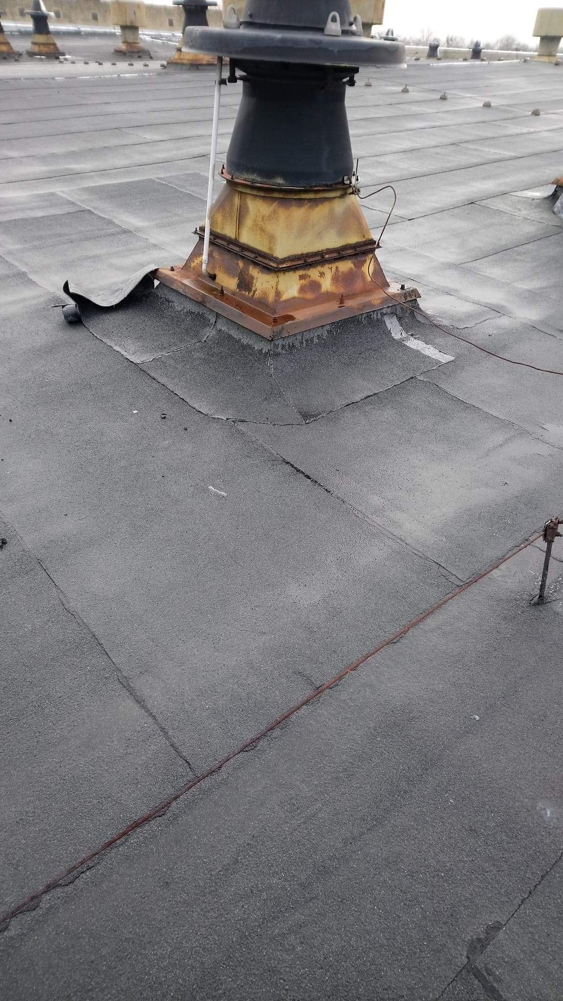 Płaski dach pokryty papą z widocznym kominem wentylacyjnym z elementami korozji oraz instalacją odgromową.