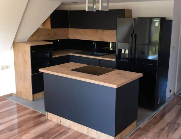Nowoczesna kuchnia w odcieniach czerni i drewna, z wyspą kuchenną i czarną lodówką Samsung, umieszczona na poddaszu.