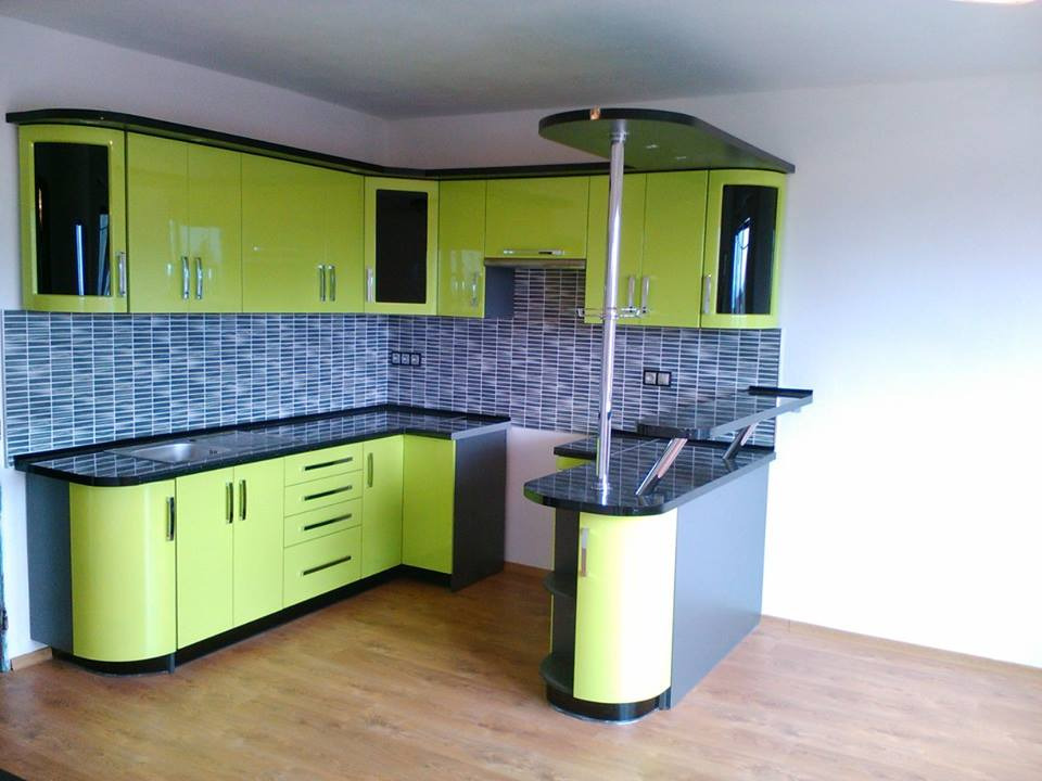 Nowoczesna kuchnia z jasnozielonymi szafkami, czarnymi blatami i barkiem z chromowanym wspornikiem na kieliszki, wykończona mozaiką na ścianie.