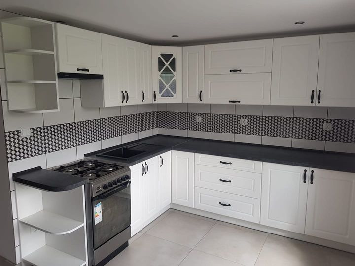 Biała kuchnia z czarnymi uchwytami i blatem, wzorzyste płytki nad blatem, widoczna kuchenka gazowa.