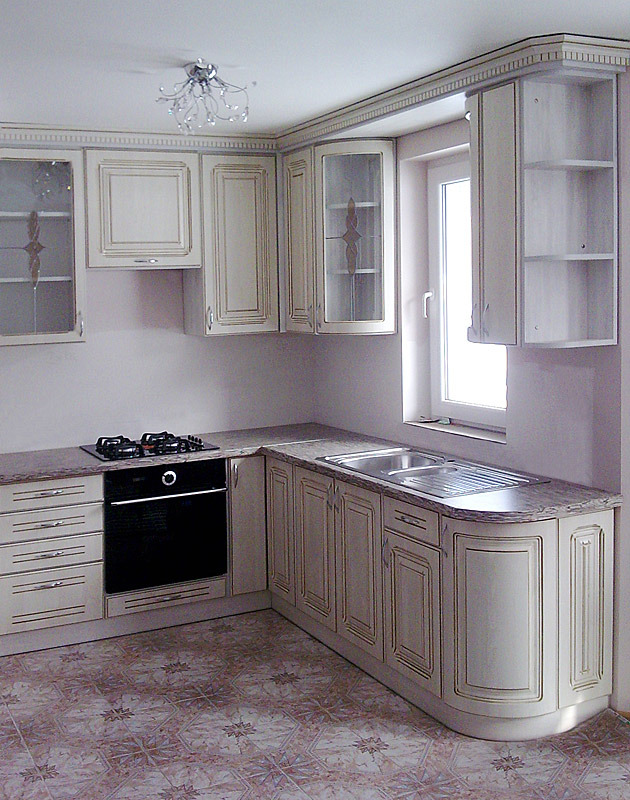 Kuchnia na wymiar w stylu klasycznym, jasne fronty z frezowanymi detalami i ciemniejszymi obwódkami, ciemny blat, płyta grzewcza, piekarnik i zlew dwukomorowy, dekoracyjny żyrandol.