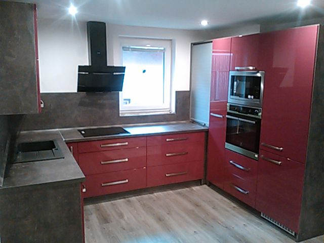 Nowoczesna kuchnia z bordowymi, lakierowanymi frontami szafek, szarym blatem i czarnym okapem nad płytą indukcyjną, z widoczną zabudową piekarnika i mikrofalówki.