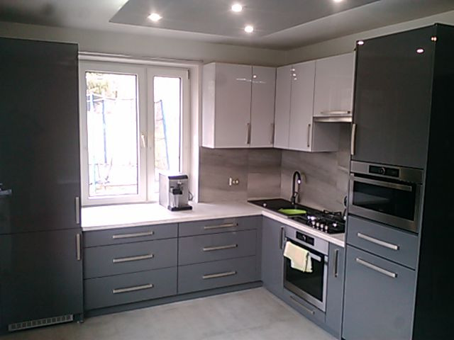 Nowoczesna kuchnia w odcieniach szarości i bieli z błyszczącymi frontami, ekspres do kawy na blacie pod oknem.