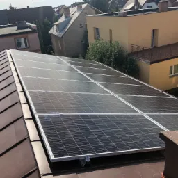 Panel słoneczny zamontowany na brązowym dachu domu jednorodzinnego w zabudowie miejskiej, widok z góry.