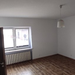 Elerk construction - Pusty pokój z drewnianą podłogą, grzejnikiem pod oknem, otwartymi drzwiami z przeszkleniami i widokiem na zewnątrz. Świeżo pomalowane ściany w odcieniach bieli, surowy stan wykończenia.