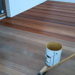 Fragment tarasu z desek kompozytowych, częściowo zabezpieczonych impregnatem, widoczny kubeł z preparatem i pędzel na kiju.