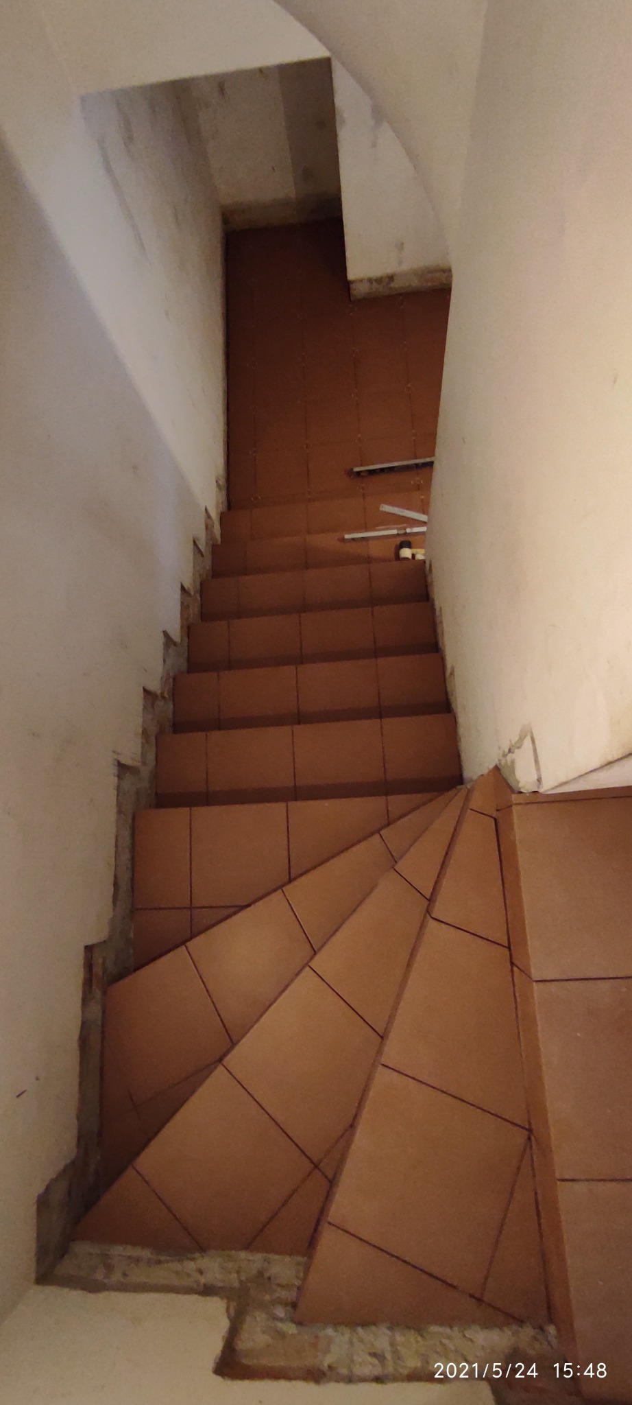 Klatka schodowa w trakcie kładzenia terakoty, widoczne niedokończone ściany i narzędzia.