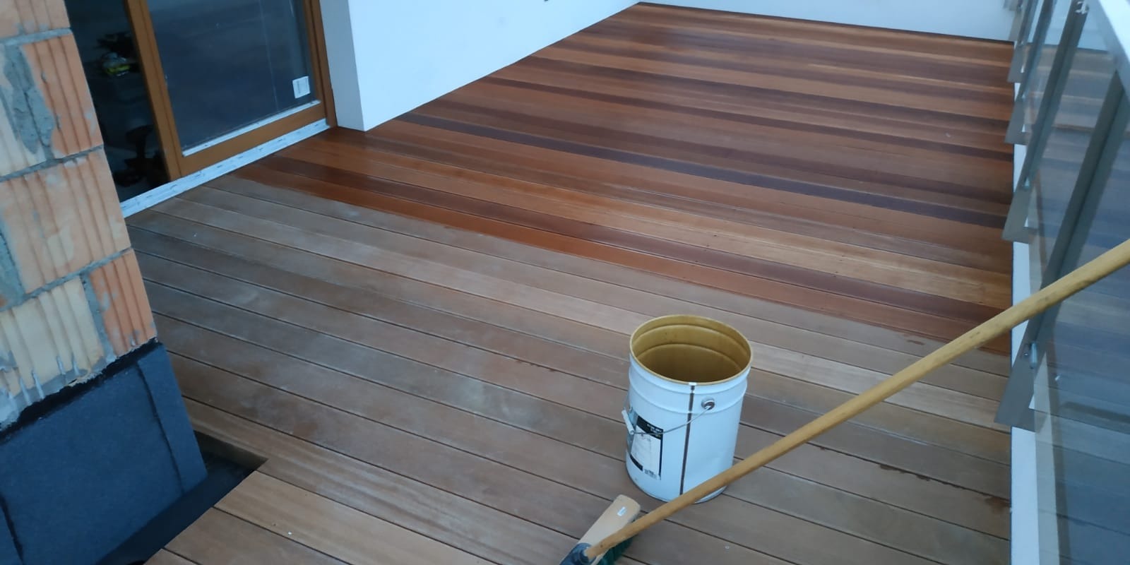 Fragment tarasu z desek kompozytowych, częściowo zabezpieczonych impregnatem, widoczny kubeł z preparatem i pędzel na kiju.