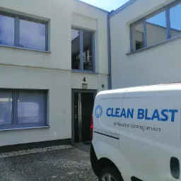 Jasny budynek z szarymi ramami okiennymi i drzwiami wejściowymi numer 4, częściowo zasłonięty przez biały samochód dostawczy z niebieskim logo 'CLEAN BLAST professional cleaning services'.