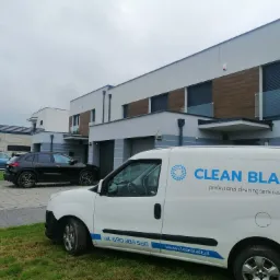 Biały samochód dostawczy z logo Clean Blast parkuje przed nowoczesnymi domami szeregowymi z drewnianymi akcentami elewacyjnymi.