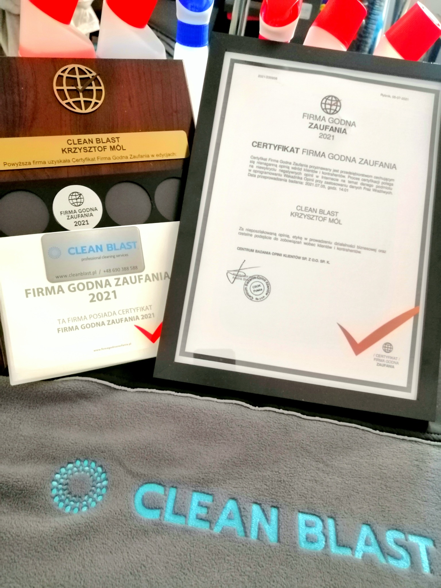 Certyfikat 'Firma Godna Zaufania 2021' firmy Clean Blast z Tychów, prezentowany obok drewnianego pudełka z logo i szarego ręcznika z nazwą firmy.