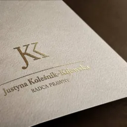 Wizytówka z tłoczonym, złotym logo i napisem 'Justyna Koleśnik-Kijewska RADCA PRAWNY' na kremowym, teksturowanym papierze, ujęcie pod kątem.