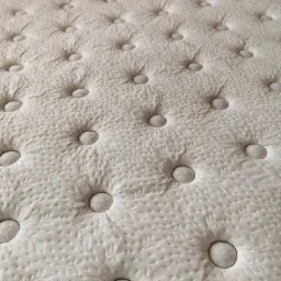 Jasny materac z regularnym wzorem pikowania i guzikami, ukazujący fakturę materiału i precyzję wykonania.