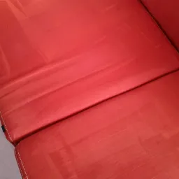 Czerwona, dwuczęściowa kanapa z widocznymi śladami po czyszczeniu na powierzchni siedziska.