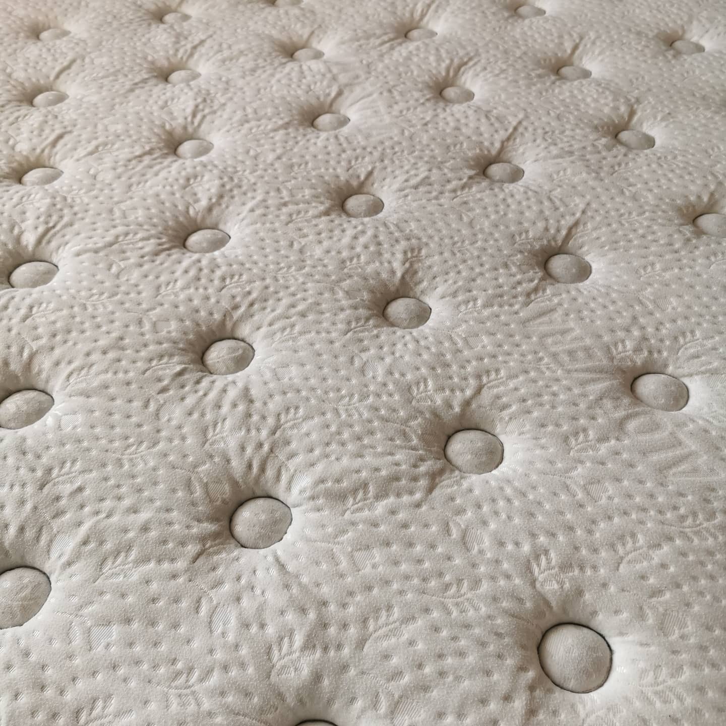 Jasny materac z regularnym wzorem pikowania i guzikami, ukazujący fakturę materiału i precyzję wykonania.