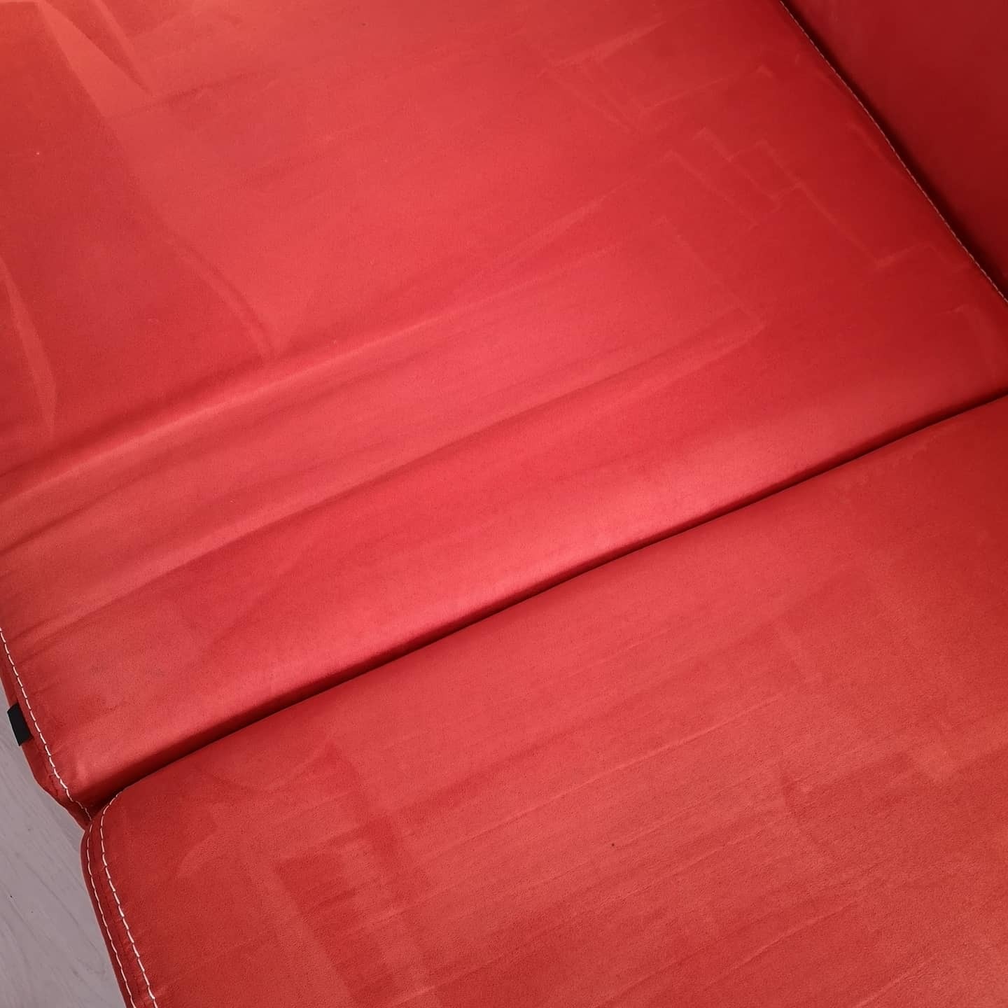 Czerwona, dwuczęściowa kanapa z widocznymi śladami po czyszczeniu na powierzchni siedziska.