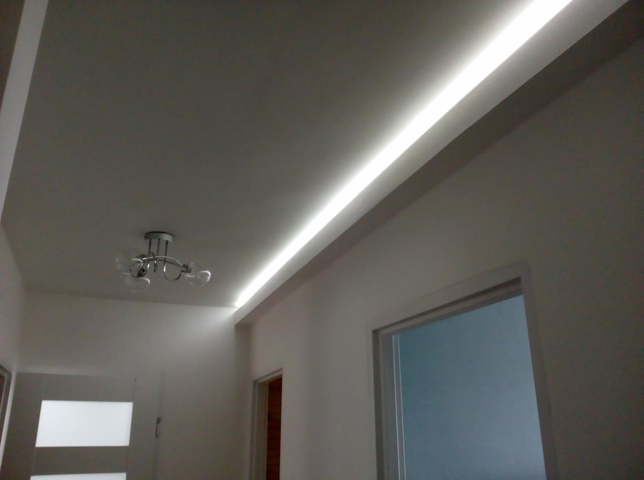 Nowoczesne oświetlenie LED zamontowane w suficie podwieszanym w mieszkaniu w Wielgiem, widoczny fragment ściany z drzwiami i lampa sufitowa.