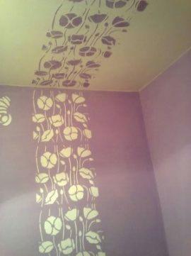 Fioletowa ściana z ręcznie malowanym wzorem kwiatowym, kontynuowanym na suficie w odcieniach beżu i fioletu, tworzącym dekoracyjny pas.