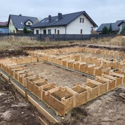 M&S-Bud - Szalunek fundamentów zbrojonych na budowie domu jednorodzinnego, widok z góry, w tle domy z ciemnymi dachami i jesienne trawy.