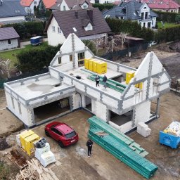 M&S-Bud - Budowa domu z bloczków Ytong w trakcie realizacji, widok z drona. Na dachu stoją dwie osoby, obok czerwony samochód i materiały budowlane.