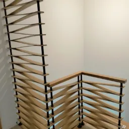 Nowoczesne schody drewniane z ażurową balustradą, wykonane w Mszanie Dolnej, z elementami z jasnego drewna i czarnymi łącznikami, widoczne z dołu.