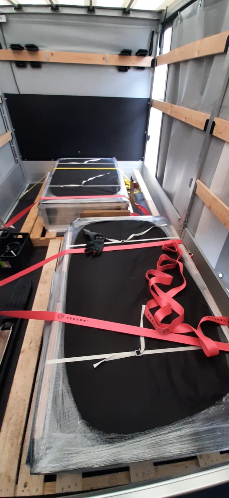 Szyby samochodowe zabezpieczone folią i pasami transportowymi na paletach wewnątrz przestrzeni ładunkowej busa.