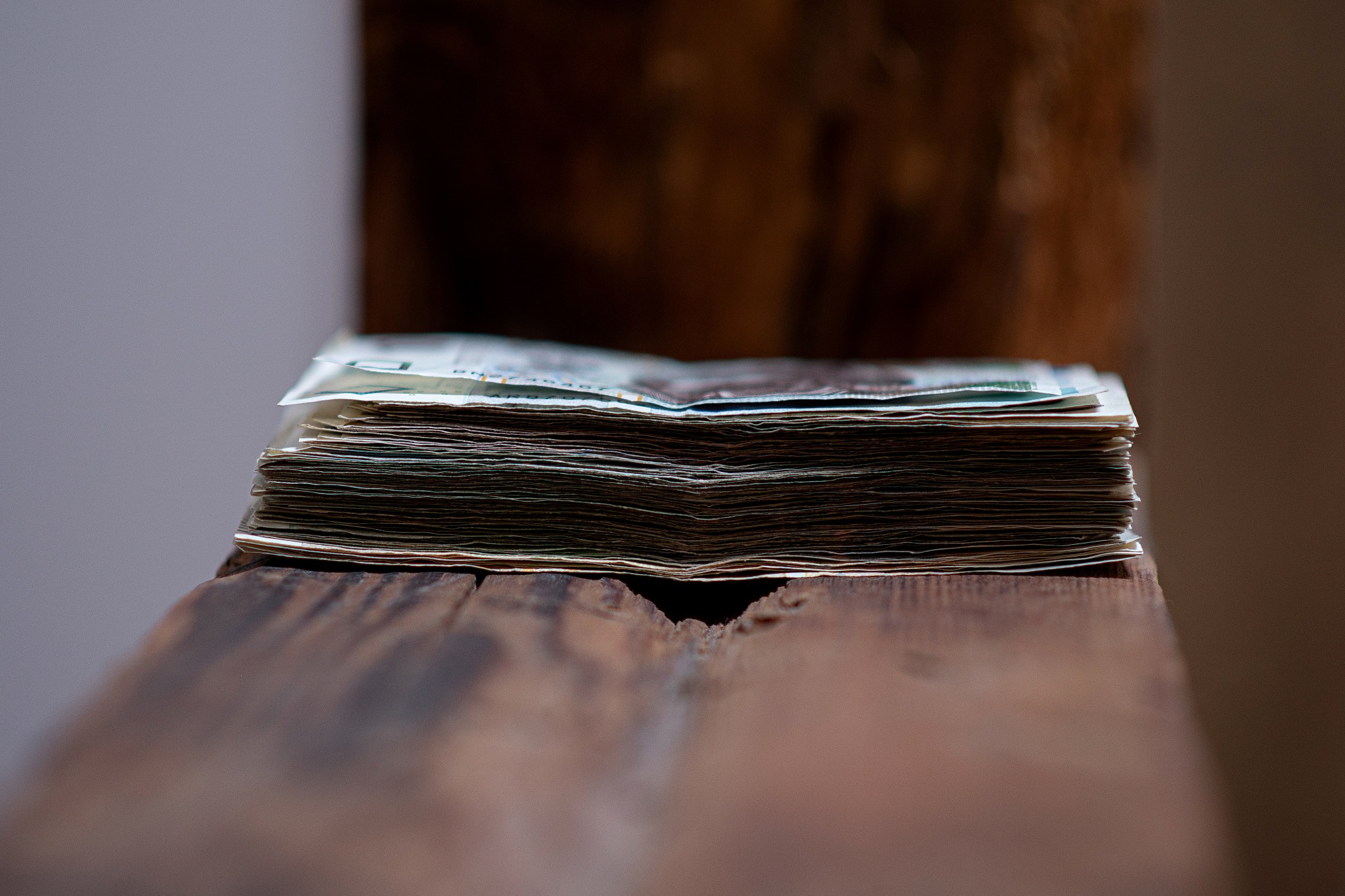 Stos banknotów leżący na drewnianej powierzchni, widoczne detale faktury drewna i krawędzi banknotów.