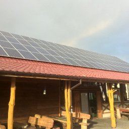 Hymon Energy sp. z o.o. - Instalacja paneli słonecznych na dachu drewnianej karczmy z czerwoną dachówką, widoczna antena satelitarna.