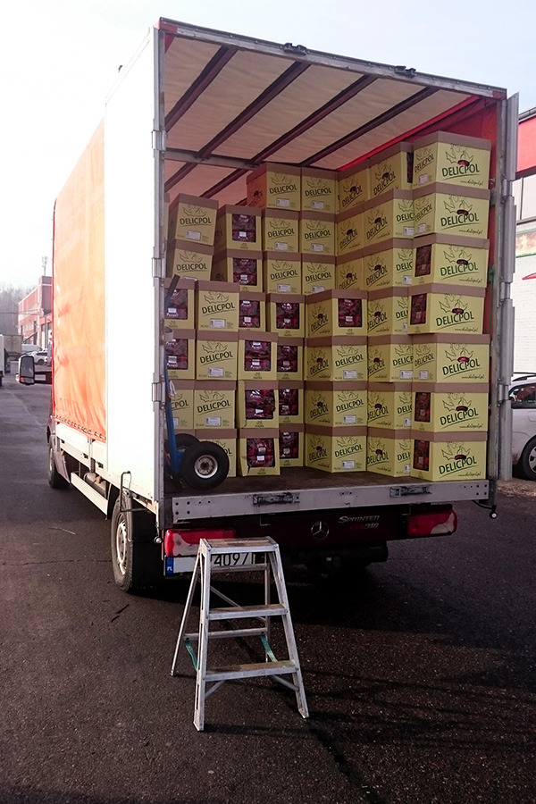 Ciężarówka Mercedes Sprinter załadowana kartonami z napisem DELICPOL, z tyłu drabina i wózek transportowy