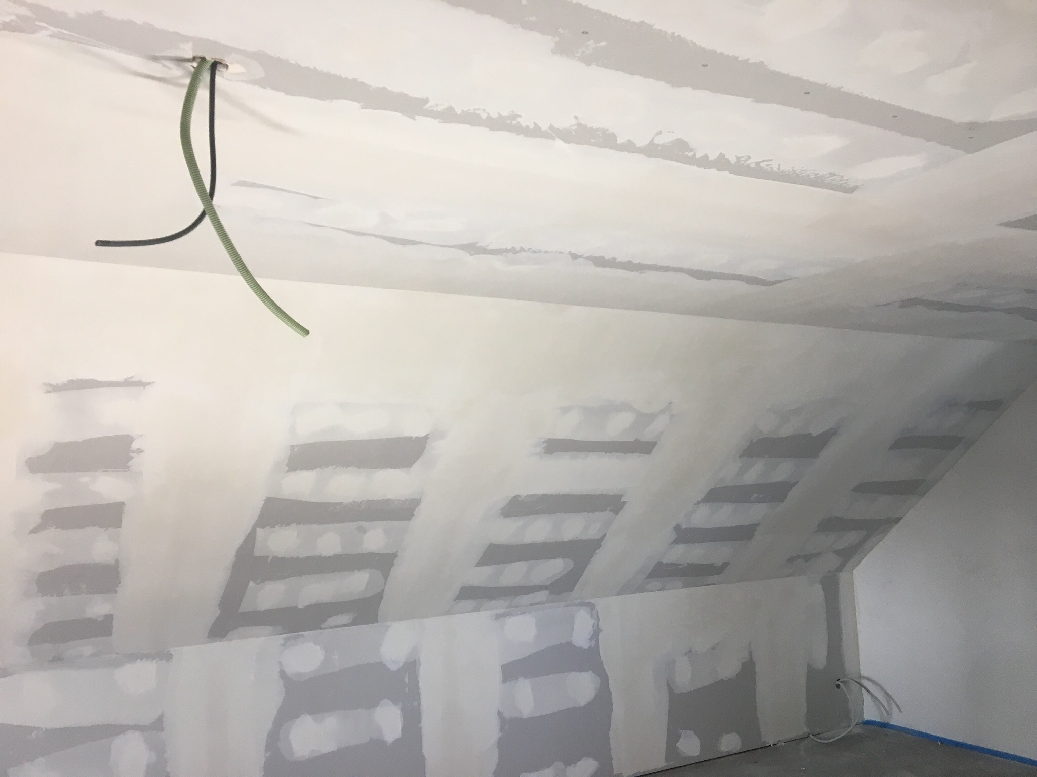 Poddasze w trakcie szpachlowania, widoczne łączenia płyt kartonowo-gipsowych na skośnym suficie i ścianach, wystające przewody elektryczne, ślady szpachli na podłodze.