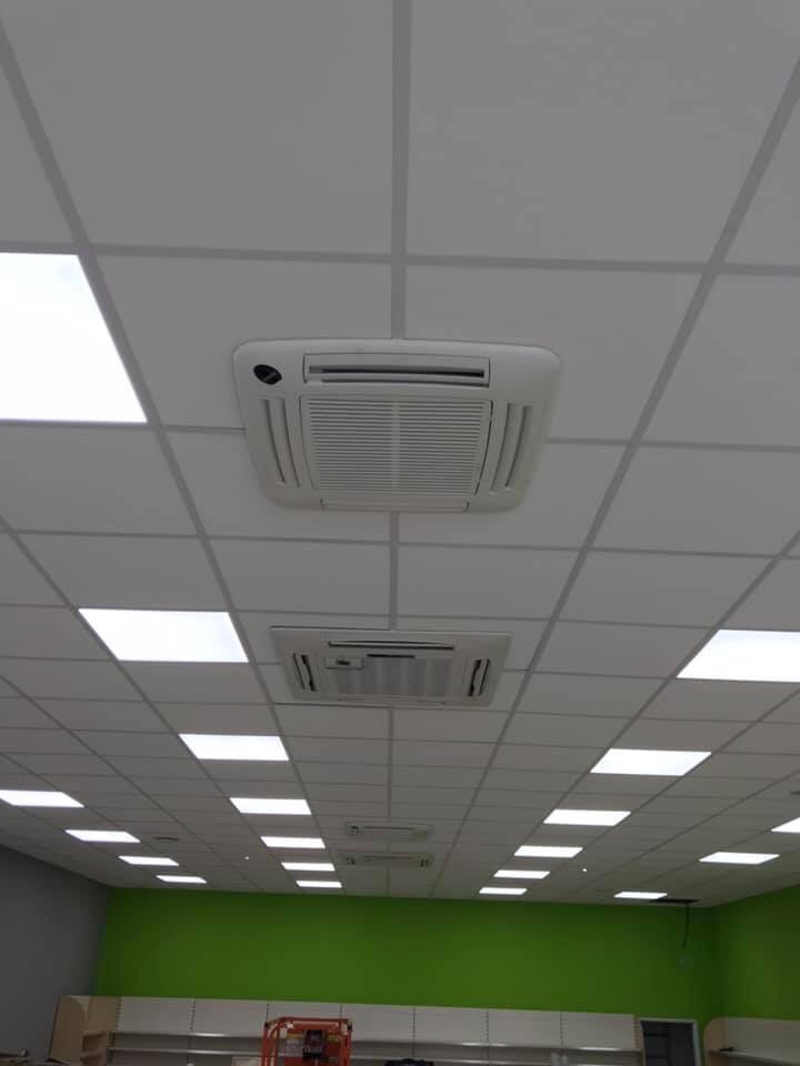 Kasetonowy sufit podwieszany z wbudowanymi panelami LED i dwoma klimatyzatorami kasetonowymi, widok z dołu w pomieszczeniu z zieloną ścianą.