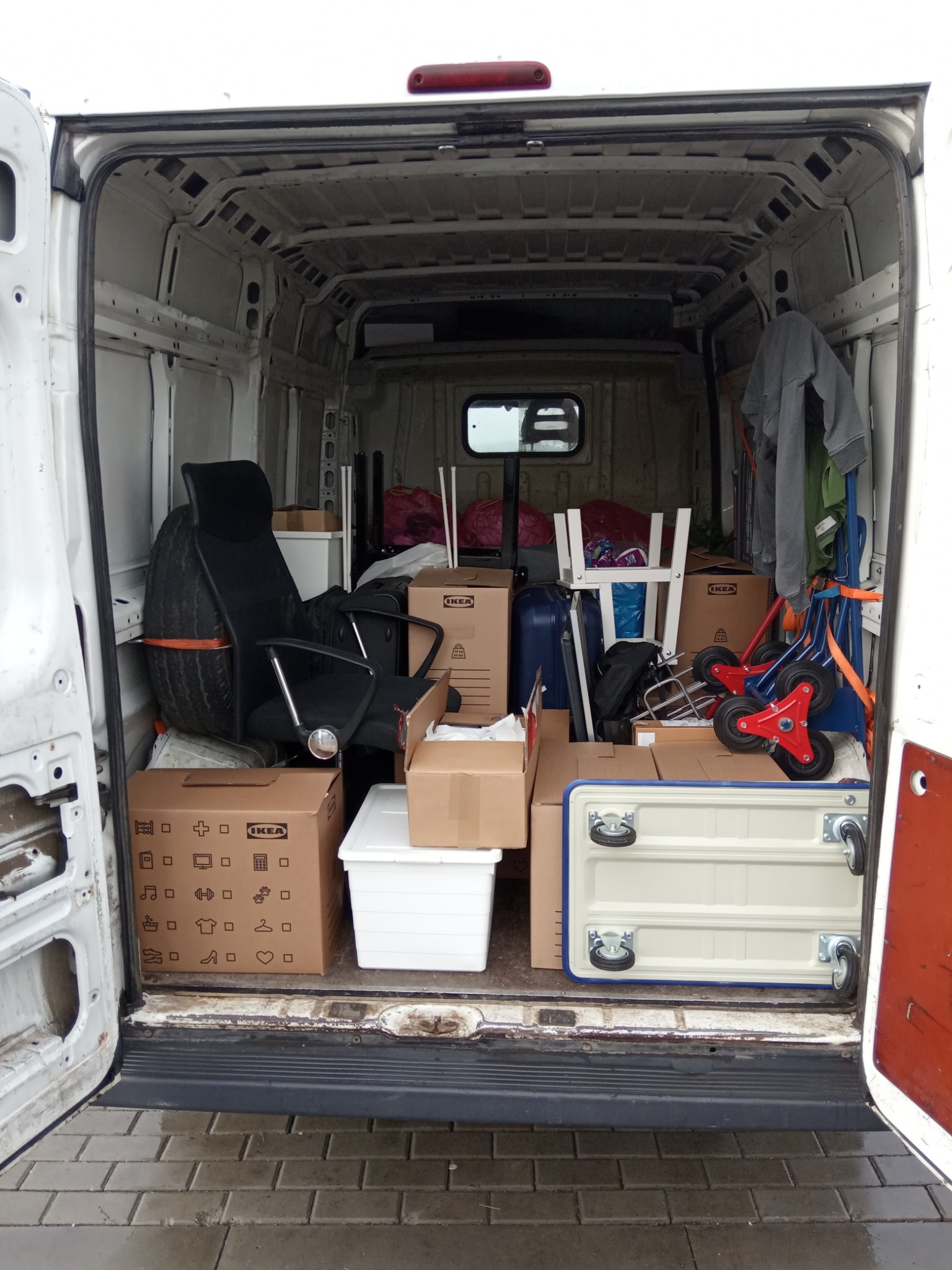 Wnętrze furgonetki załadowane kartonami IKEA, krzesłem biurowym i innymi przedmiotami, przygotowane do transportu.