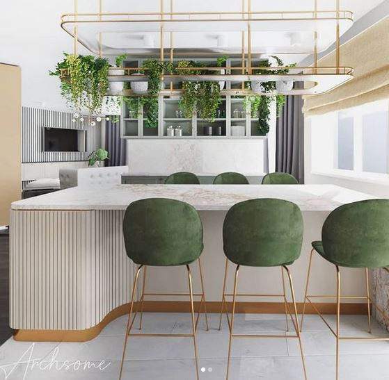 Wnętrze kuchni z wyspą, marmurowym blatem, zielonymi hokerami na złotych nogach i wiszącą konstrukcją z roślinami doniczkowymi.