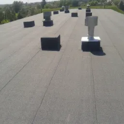 Widok z góry na płaski dach pokryty papą termozgrzewalną z kominkami wentylacyjnymi i obróbkami blacharskimi, Nasielsk.