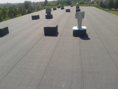 Widok z góry na płaski dach pokryty papą termozgrzewalną z kominkami wentylacyjnymi i obróbkami blacharskimi, Nasielsk.