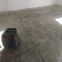 Przygotowanie podłoża pod posadzkę: szlifowanie betonu z użyciem odkurzacza przemysłowego Metabo ASR 25 L SC, widoczne ślady po szlifowaniu i kable zasilające.