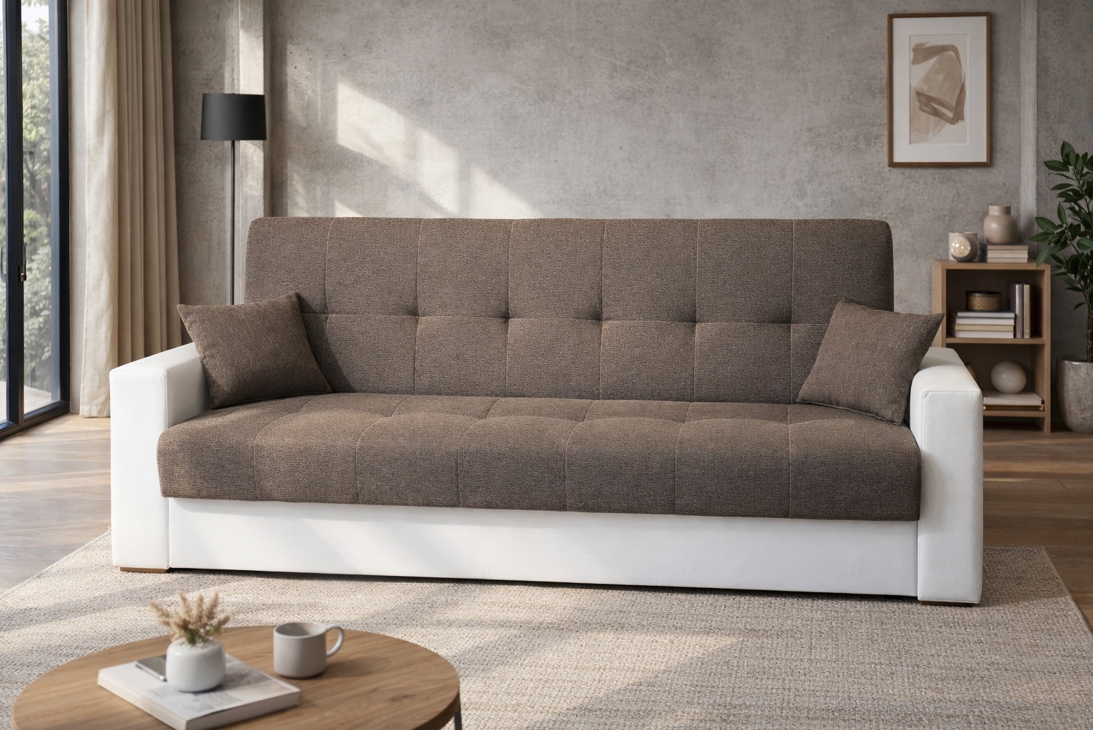 Rozkładana sofa z brązową tapicerką i białymi bokami, uzupełniona poduszkami. Na stoliku kawa i dekoracje, w tle betonowa ściana i regał z książkami.