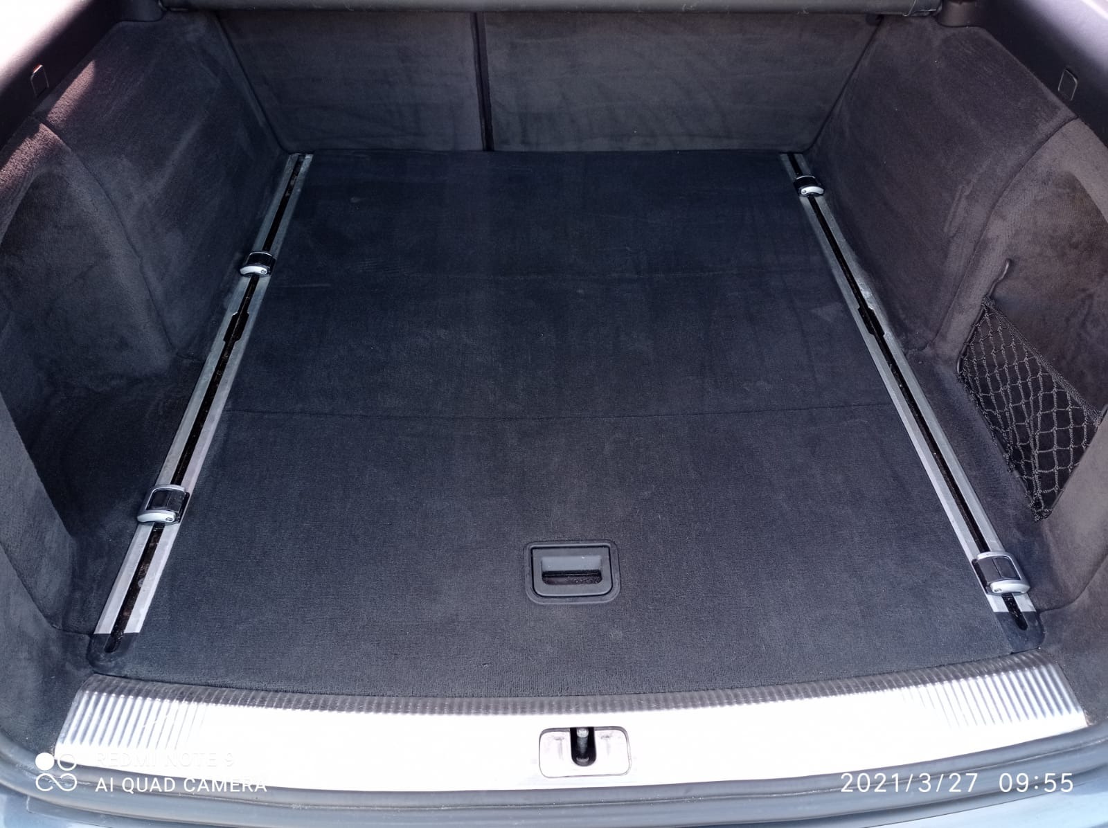 Czysty bagażnik samochodu kombi z czarną wykładziną, metalowymi szynami i siatką po prawej stronie.