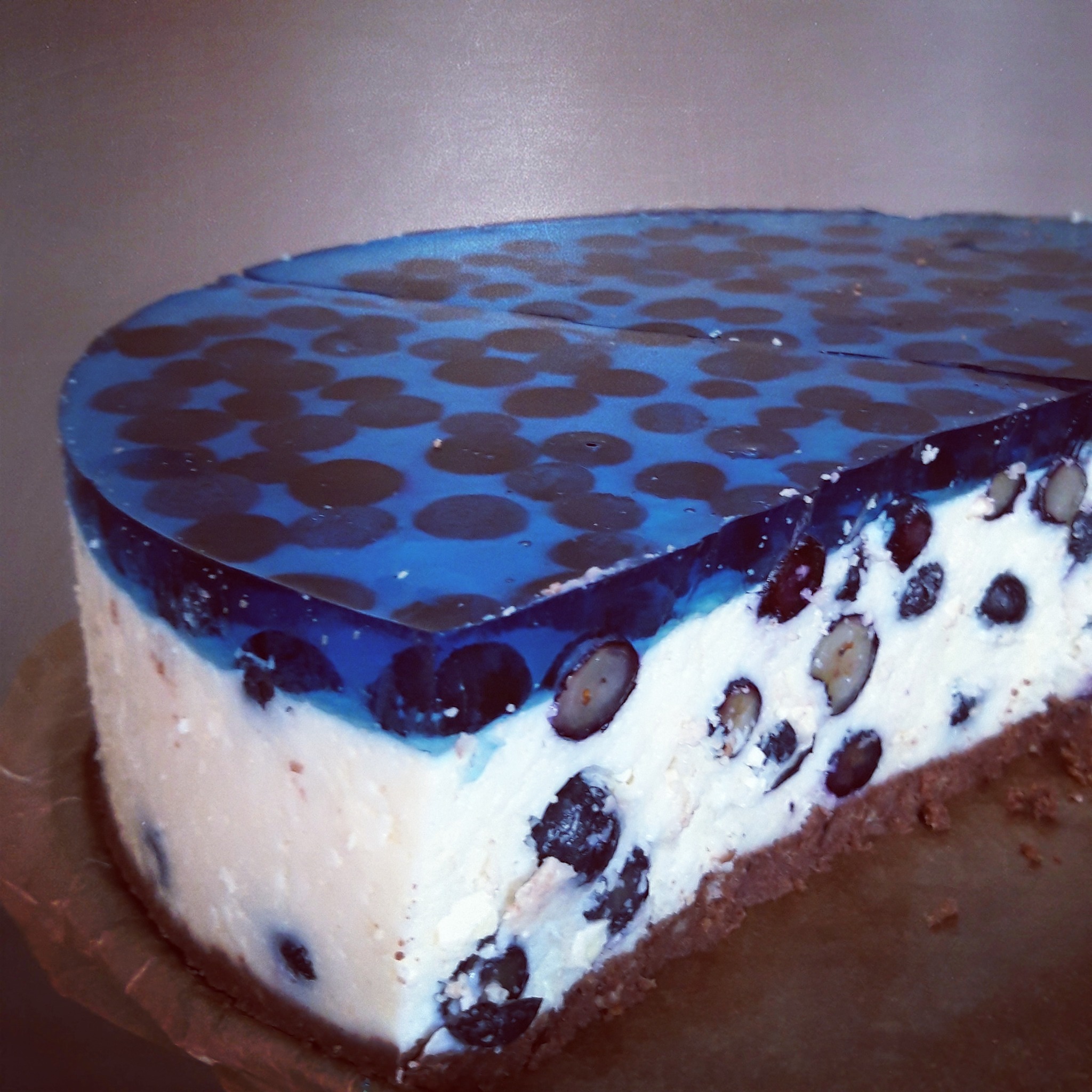 Kawałek sernika na zimno z borówkami i galaretką o smaku jagodowym, na czekoladowym spodzie, ułożony na papierze do pieczenia.