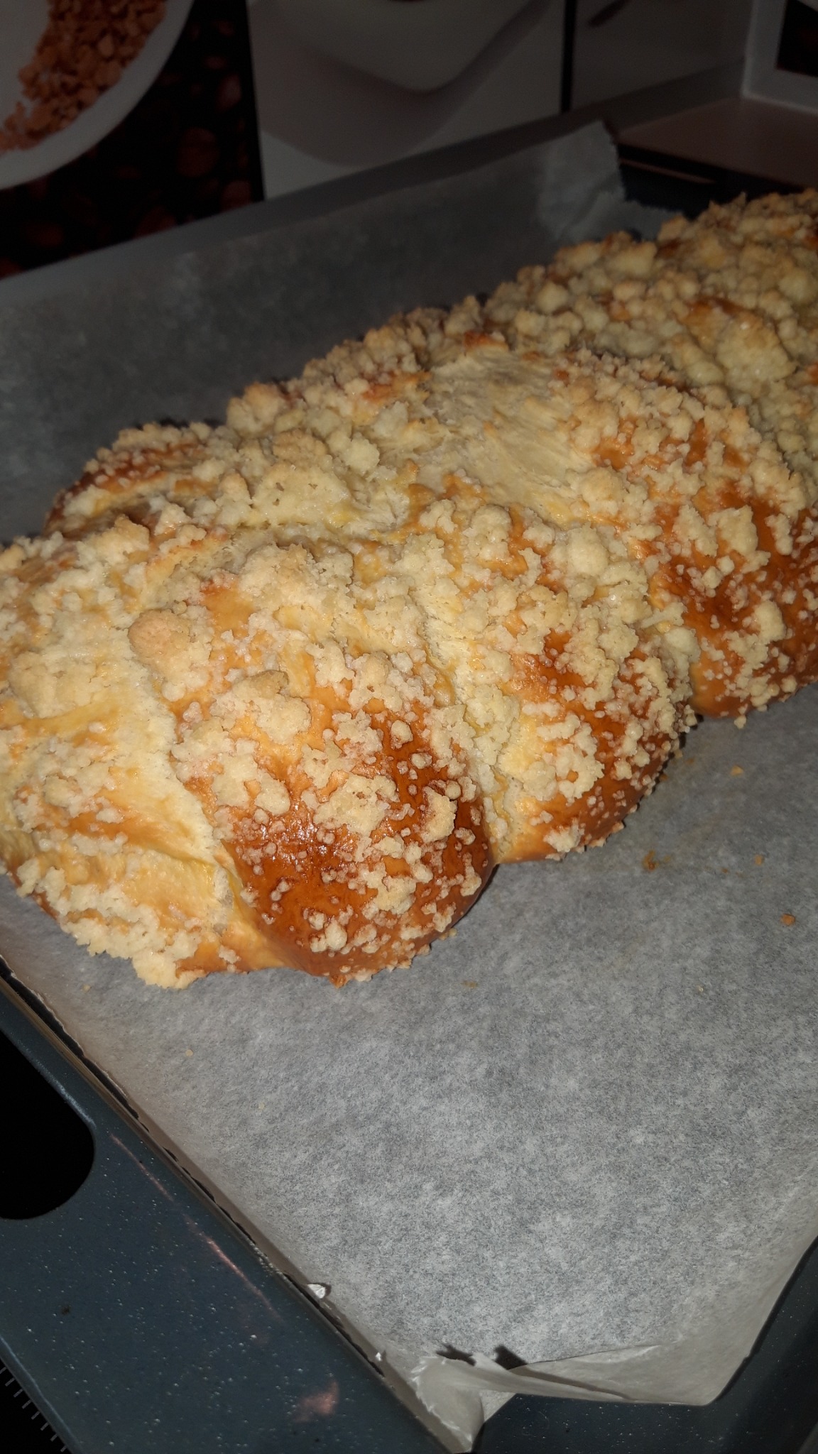 Świeżo upieczona, złocista chałka z kruszonką na papierze do pieczenia, leżąca na blasze.