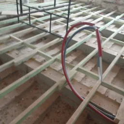 Konstrukcja podłogi z drewnianych legar&oacute;w, widoczne rury instalacji grzewczej i elementy metalowej konstrukcji w surowym wnętrzu.